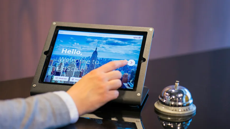 Hotel guest checking in on a front-desk tablet beside a reception bell